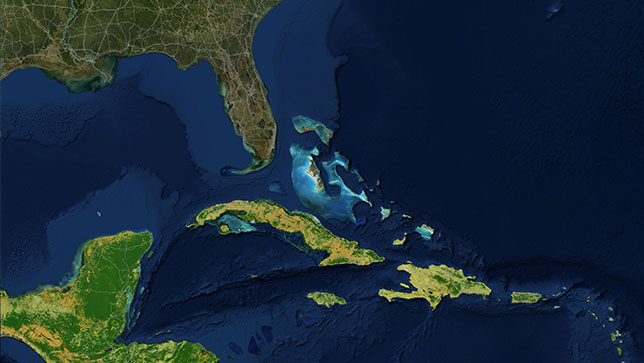 An area in the Caribbean Sea with islands illuminated in yellow and green, and some water areas near the Florida Keys illuminated in shades of brighter blue than the surrounding ocean
