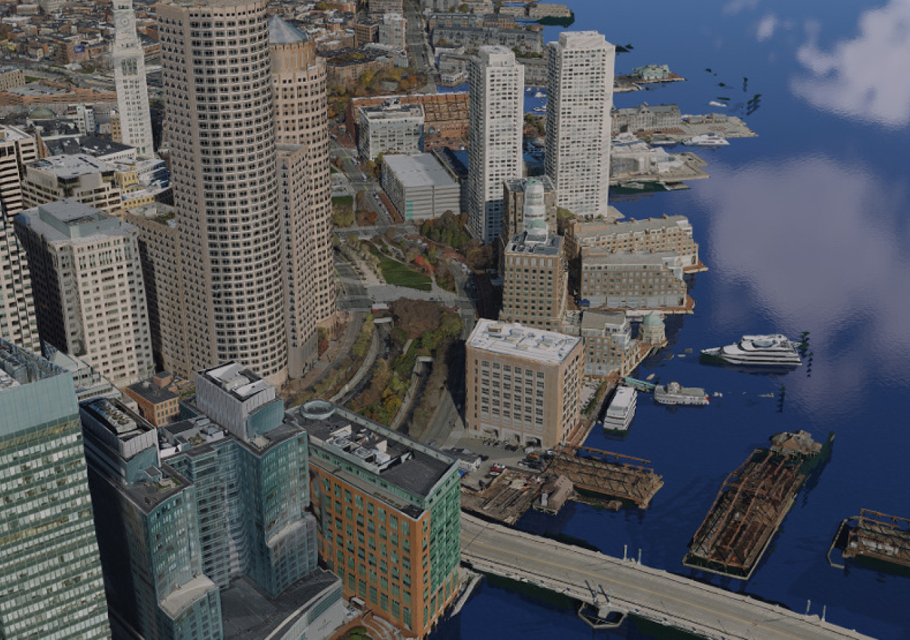 Aerial image of a city along the water with tall buildings and boats and barges in the blue water