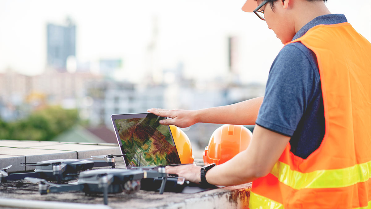 An on-site worker in a yellow safety vest connects a drone to a laptop,An on-site worker in a yellow safety vest connects a drone to a laptop