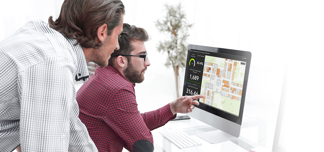 Two men looking at a computer screen showing a blue and pink map representing GIS data for indoor space planning