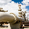 A large white aboveground gas pipeline beside related equipment in a desert landscape under a cloud-swept bright blue sky