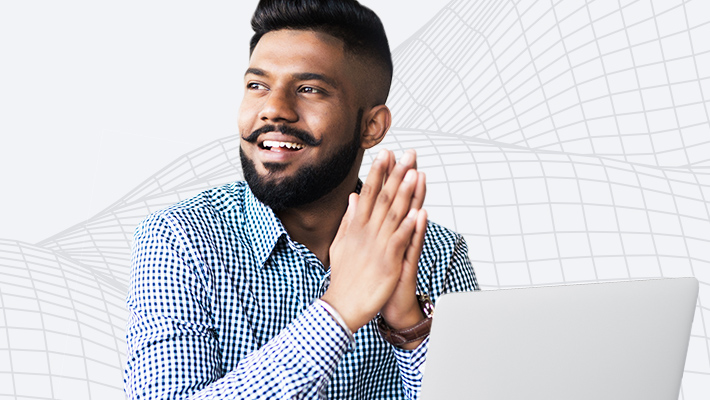 A person in a checkered button-down shirt and styled moustache using a laptop and smiling