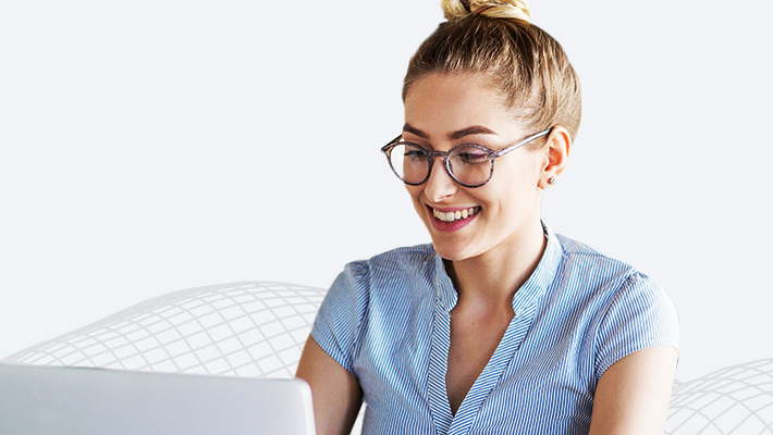 A person in a pale blue blouse and glasses smiling at an open laptop