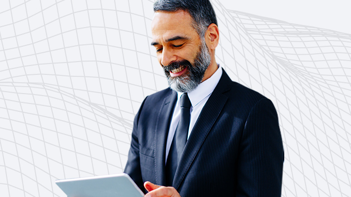 A smiling bearded person wearing a navy blue suit and using a laptop