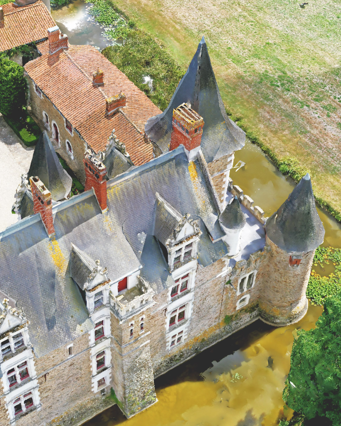 Een dronefoto van een kasteelachtig landgoed met een binnenplaats, omgeven door een gracht en uitgestrekte landbouwvelden.