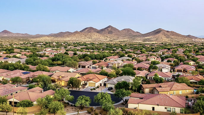 A large neighborhood with orange roofed houses with mountains in the background and green trees