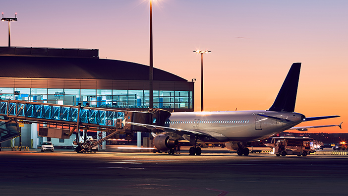 Airport with large glass windows at dusk and a commercial airplane on a runway