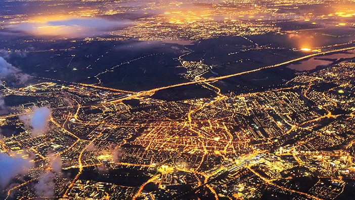 Picture of an urban city at nighttime with bright yellow lights and a bridge over blue water