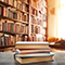 A stack of four books sitting on a wooden tabletop with a sunlit library in the background