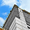 An image of a concrete building under construction beside a tower crane, taken from the ground looking up toward a bright blue sky