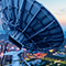 An aerial image of a sleek modern city lit up for sunset with a large satellite dish in the foreground