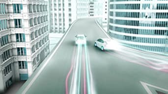 Two Prius' driving down modern city street with neon trailer lights showing driving path.