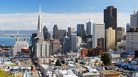 The San Francisco skyline with tall buildings, a blue sky, and blue water in the bay