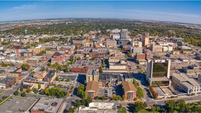 An aerial view of the City of West Fargo, North Dakota with a blue sky, trees, and clustered buildings