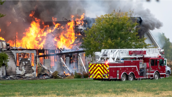 A house fire with orange flames coming from the roof and gray smoke and a red fire truck next to the home