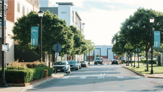 A neighborhood street flanked by residential buildings, cars, and trees