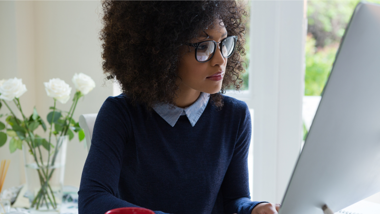 A woman working on her desktop computer and looking at a large monitor