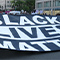 People wearing masks and holding a large Black Lives Matter sign in the middle of a crowded street 
