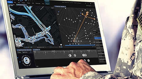 A close-up photo of a laptop screen displaying several maps while in use by a person wearing gray Army fatigues