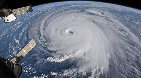 A satellite photo taken from space showing the top of a swirling tornado over blue ocean with the curvature of the Earth visible in the background 