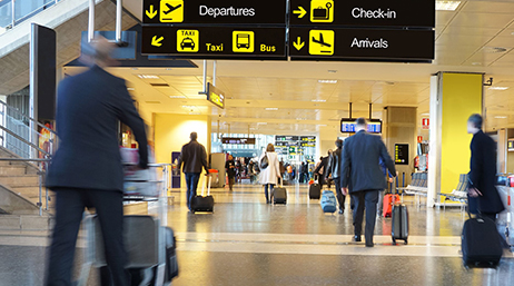 A busy airport terminal with many people walking in a wide hallway with wheeled suitcases