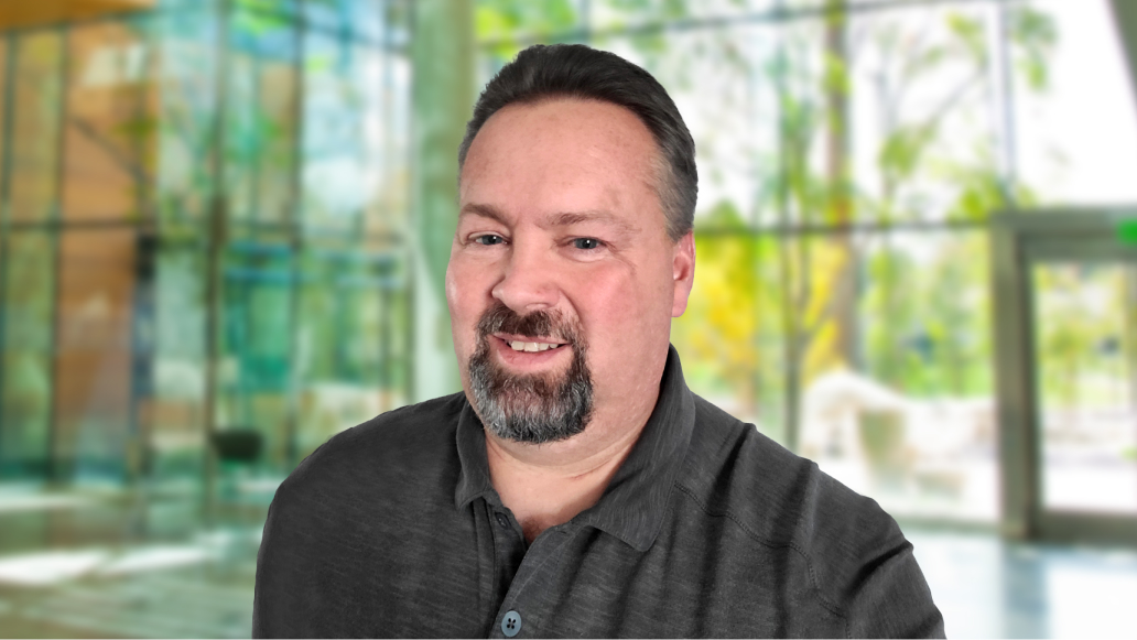 Duane Holt smiling and wearing a grey dress shirt in a modern glass building