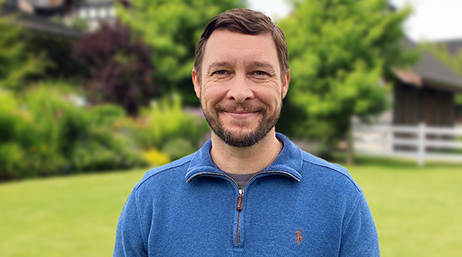 Mike Bowen wearing a blue half-zip sweater, smiling and standing outside