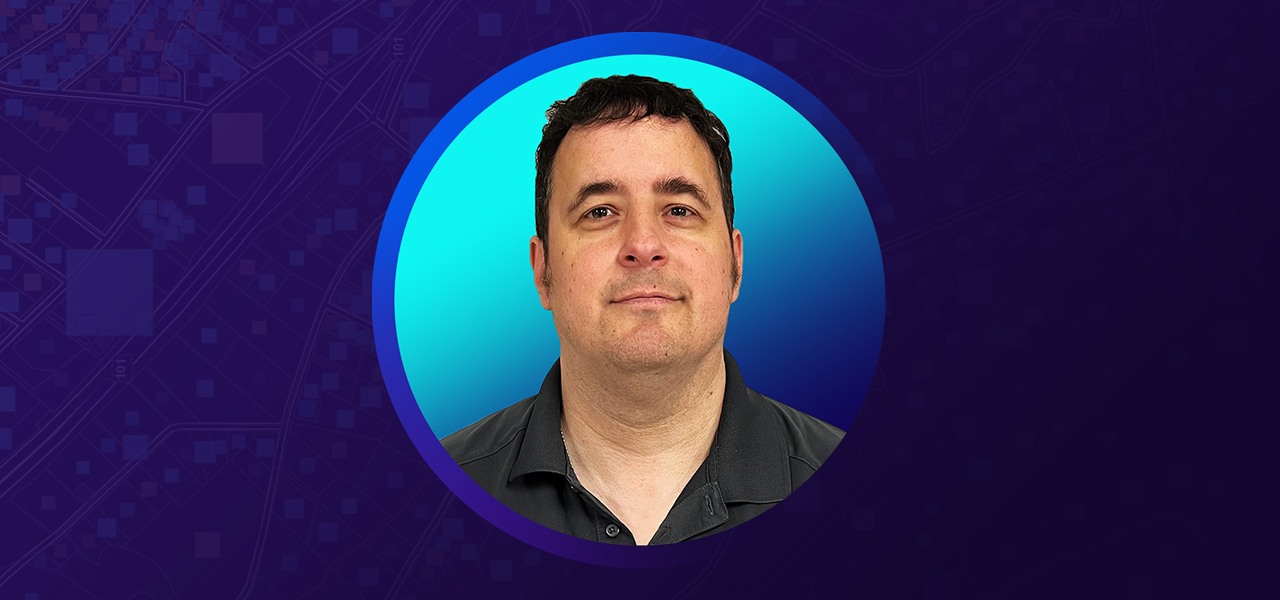 Mark Rees smiling and wearing a black collared shirt overlaid on a blue and purple bakground