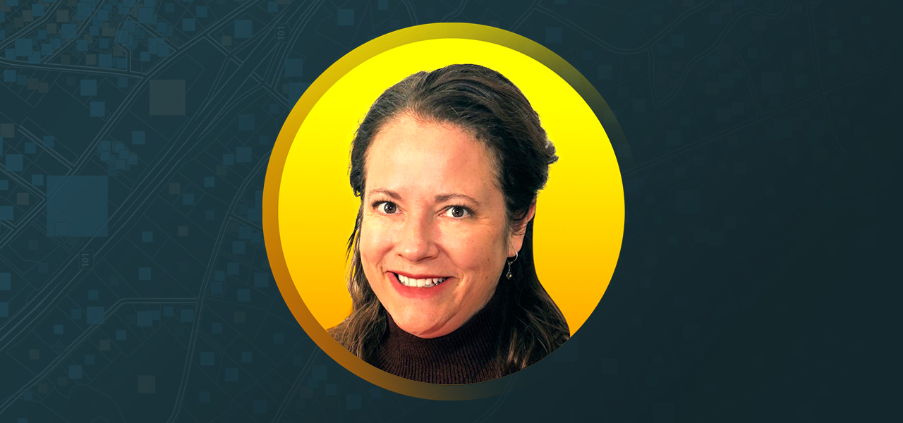 Amanda O'Shea wearing a dark turtleneck and smiling with an abstract blue and yellow background
