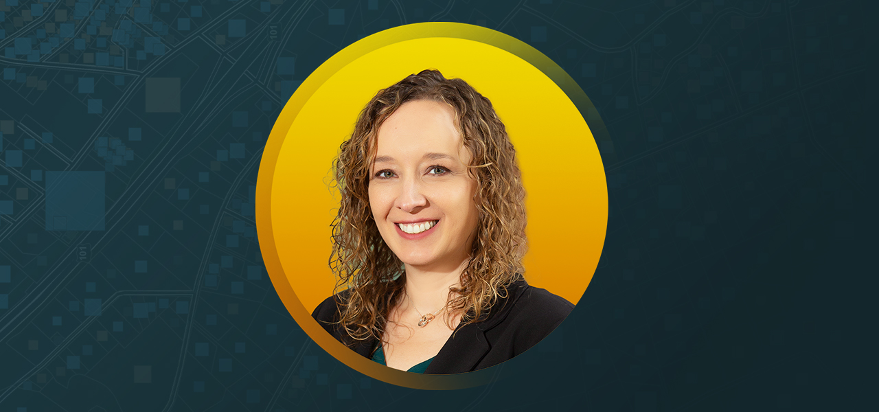 Jodie Gosselin wearing a black blazer and smiling with an abstract blue and yellow background
