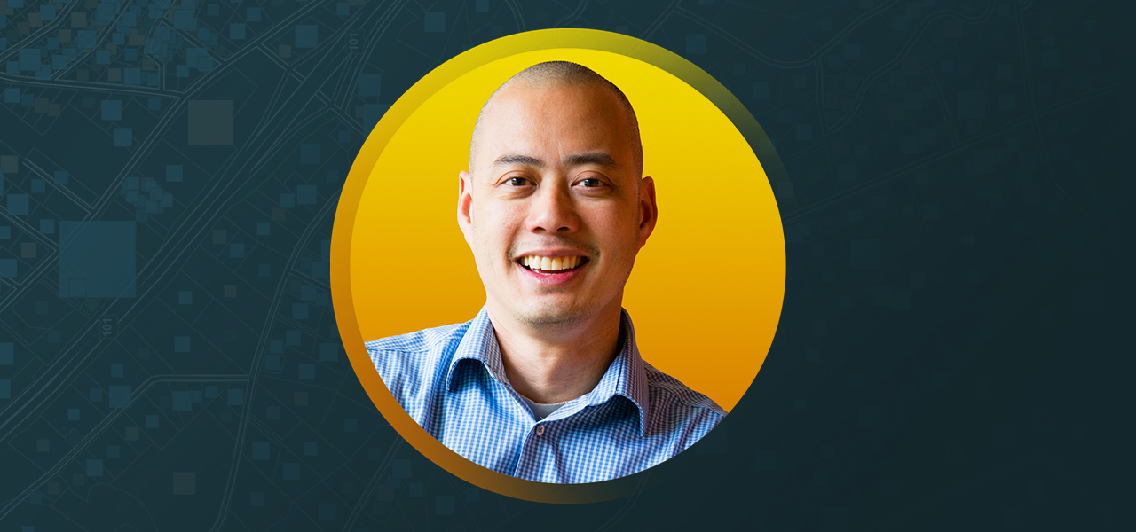 Sheng Tan wearing a blue dress shirt and smiling with an abstract blue and yellow background