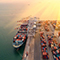 A barge carrying shipping containers docked at a seaport with many groups of stacked, multicolored containers