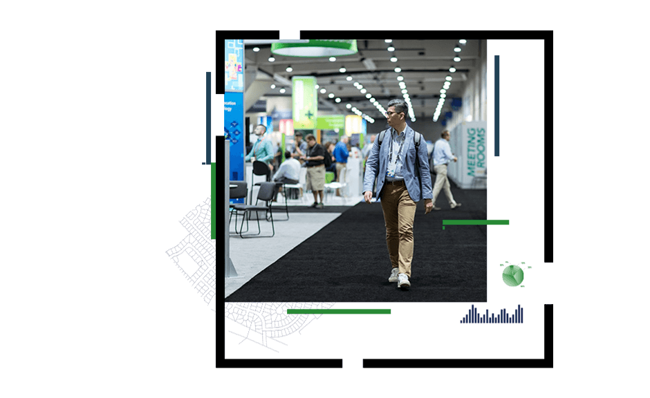 A photo of a person wearing a blue blazer and a backpack walking through a brightly lit conference exhibit hall with many booths 