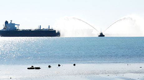 A view of a large and small ship on the ocean, with the smaller ship shooting out water from both sides