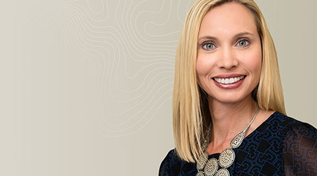 Portrait of a blonde woman wearing a black and blue blouse and a silver, circular statement necklace