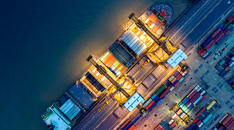 An aerial photo of a container barge alongside a loading dock with crates in many colors against a dark blue ocean