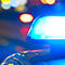 A photo of the windshield of a car reflecting a bright streetlight with out-of-focus blue and red police lights twinkling in the background
