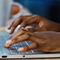 A close-focus photo of a pair of hands typing on the keyboard of a sleek laptop