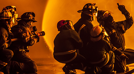 An orange-tinged photo of five firefighters pointing several hoses at a blaze