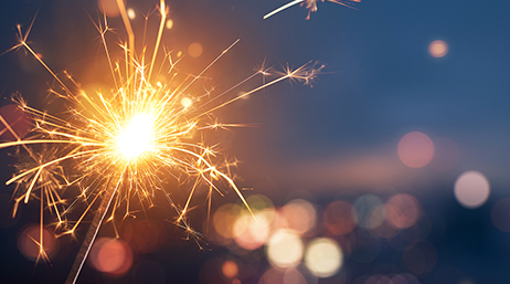 A composite image of a blazing sparkler beside a blurry image of nighttime city lights at a distance