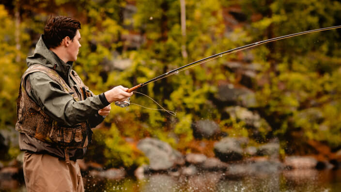 A young person wearing a camouflage vest, fishing in a forest