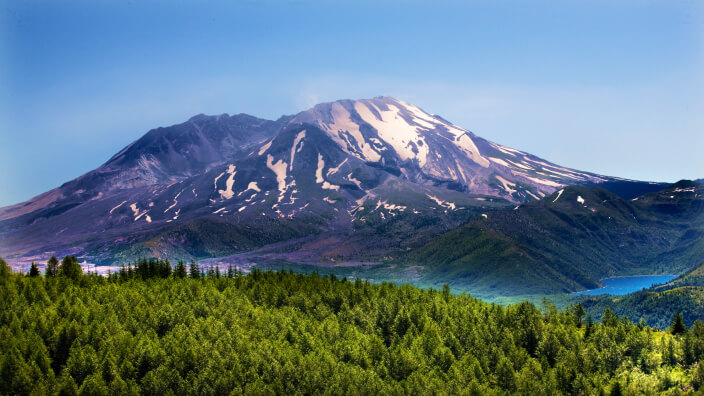 A snowy mountain and a lush green forest separated by a river