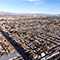 An aerial image of a sprawling suburb in brown and white with a large skyscraper-filled city in the distance beneath a clear blue sky