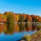 A rippling blue lake reflecting vivid orange and gold autumn trees along its banks beneath a clear blue sky