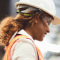 A closeup photo of a smiling person in a hardhat, safety goggles, and safety vest