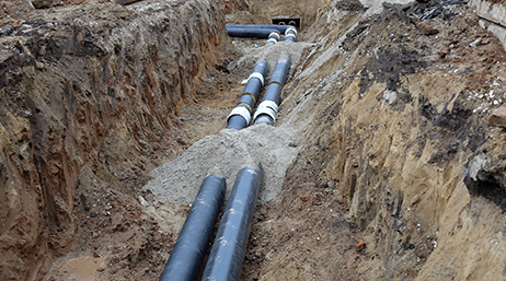 Two parallel black pipelines in an open dirt trench overlaid with a play button