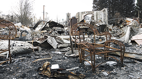 A burned down structure, chair, and charred ground from a fire in California