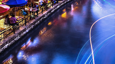 Outdoor seating along a water canal with tables and shade where people are sitting together