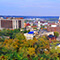 A landscape view of Dubuque, Iowa with bright colored homes, green trees, and factories on a waterfront