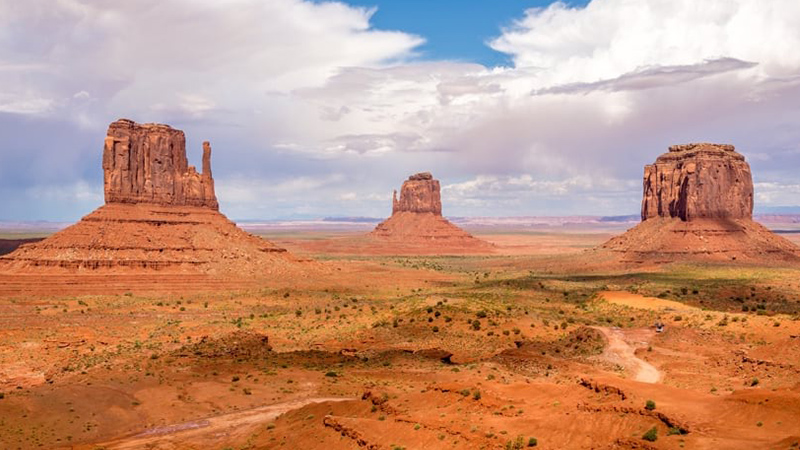 Three towering sandstone buttes under a blue cloudy sky
